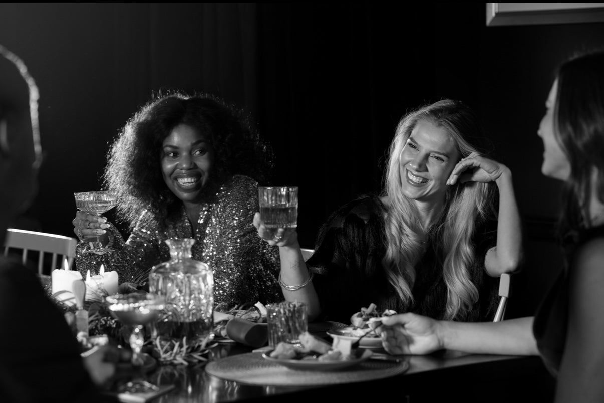 Black and white photo of people sitting around a table with drinks and food.